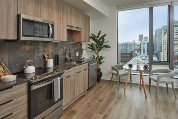 Apartment kitchen with stainless steel appliances, dining and living room with wood-style flooring.