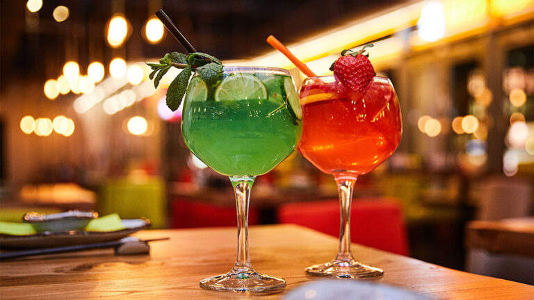 Bright red and green cocktails garnished with fruit.