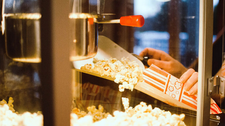 Person scooping popcorn into red striped bag.