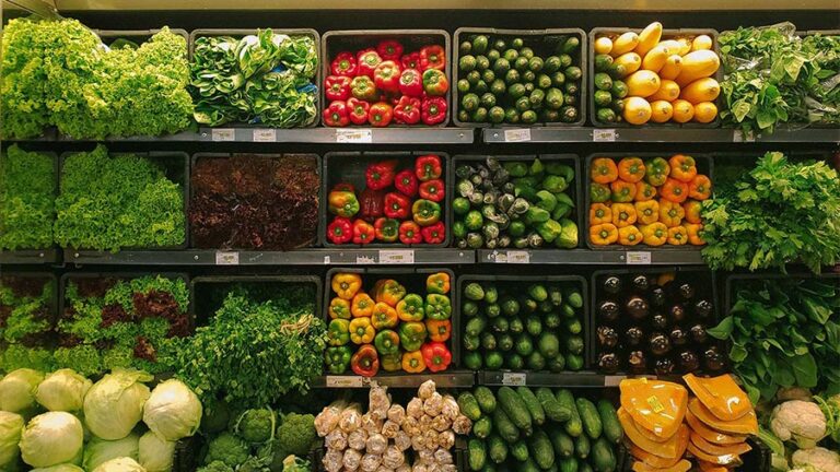 Produce section at grocery store with peppers, zucchini, and lettuce.
