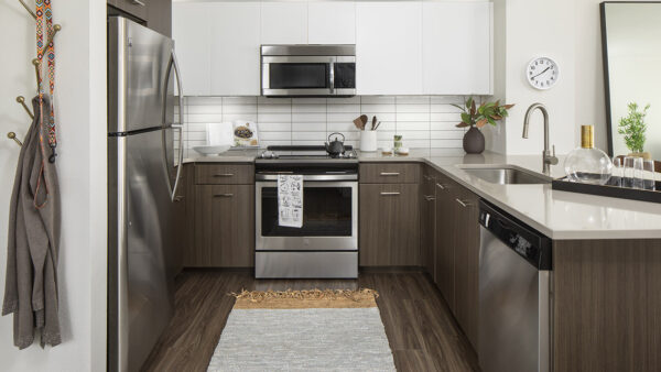 Apartment kitchen with stainless steel appliances, quartz countertops, and wood-style flooring.