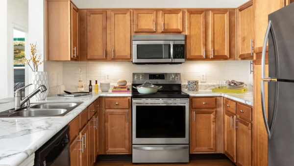 Apartment kitchen with stainless steel appliances, wood-style flooring, and marble-style countertops (shown here). Quartz-style countertops are available in select homes.