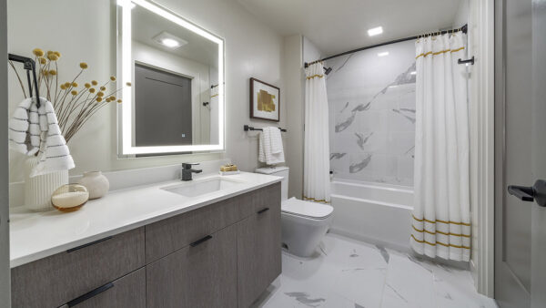 Apartment bathroom with large soaking tub, tile flooring, and LED vanity mirror.