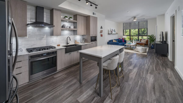 Apartment kitchen with stainless steel appliances, dining and living room with wood-style flooring.