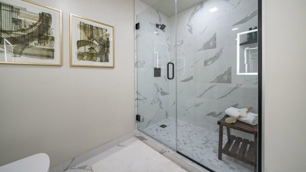 Apartment bathroom with glass-enclosed shower, tile flooring, and LED vanity mirror.