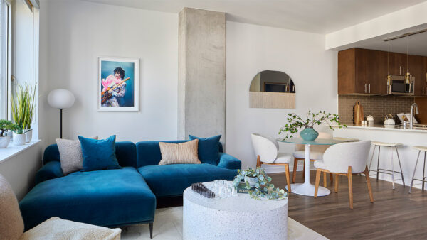 Apartment kitchen with stainless steel appliances, dining and living room with wood-style flooring.