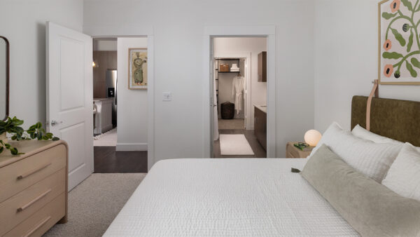 Spacious apartment bedroom with a large closet, attached bathroom, and plush carpet flooring.