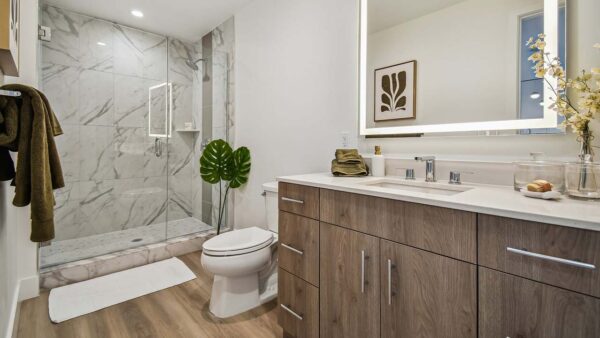Griffis West Palm apartment bathroom with wood style floor, lighted mirror, and tiled glass wall shower.