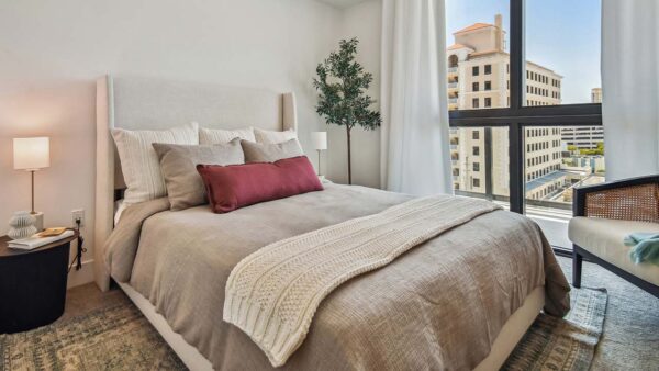 Griffis West Palm apartment bedroom with pattern rug, plush bed with headboard, and large window.