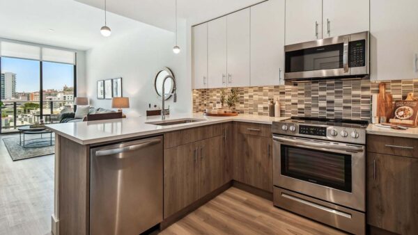 Griffis West Palm apartment kitchen with wood style floor and cabinets, tiled backsplash, and stainless steel appliances.